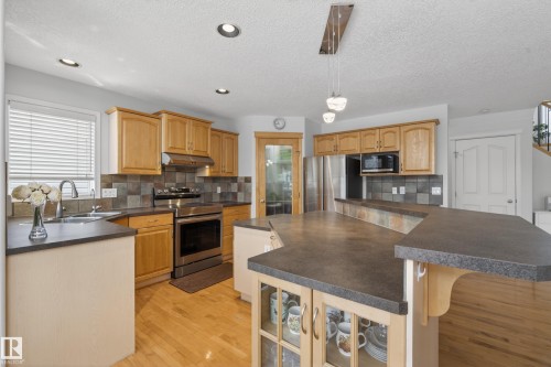 The kitchen features wood cabinetry, stainless steel appliances, a large island with a dark countertop, and hardwood flooring - 1119 Rutherford Close, Edmonton, AB - Indoor Photo Showing Kitchen With Double Sink