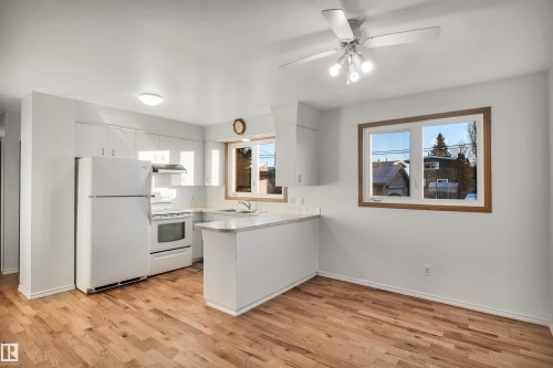 Kitchen featuring white appliances, light countertops, white cabinets, a peninsula, and light wood-style floors - 11231 41 Avenue, Edmonton, AB - Indoor Photo Showing Kitchen