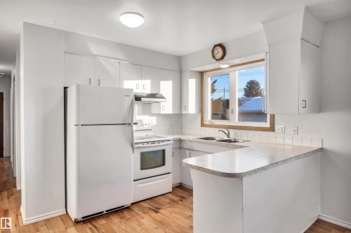 Kitchen featuring white appliances, a peninsula, white cabinets, light wood-type flooring, and light countertops - 11231 41 Avenue, Edmonton, AB - Indoor Photo Showing Kitchen With Double Sink