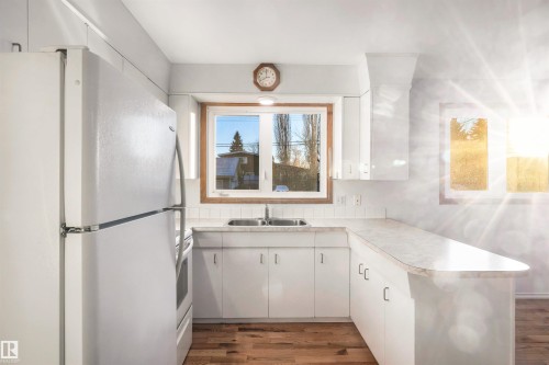 Kitchen with white appliances, white cabinets, light countertops, dark wood finished floors, and a peninsula - 11231 41 Avenue, Edmonton, AB - Indoor Photo Showing Kitchen With Double Sink