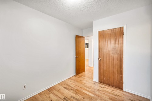 Unfurnished bedroom with a textured ceiling, light wood-style floors, and a closet - 11231 41 Avenue, Edmonton, AB - Indoor Photo Showing Other Room