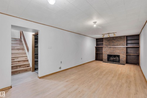 Unfurnished living room featuring light wood-style floors, stairway, a fireplace, built in features, and ornamental molding - 11231 41 Avenue, Edmonton, AB - Indoor With Fireplace