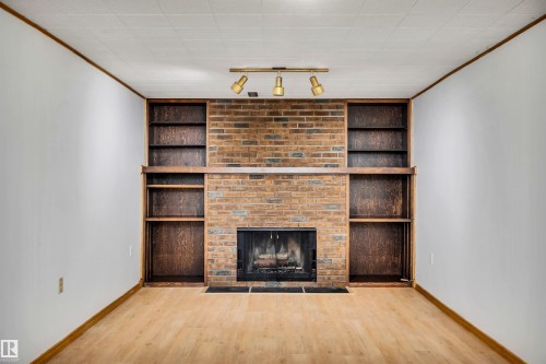 Unfurnished living room featuring built in shelves, crown molding, track lighting, wood finished floors, and a fireplace - 11231 41 Avenue, Edmonton, AB - Indoor With Fireplace