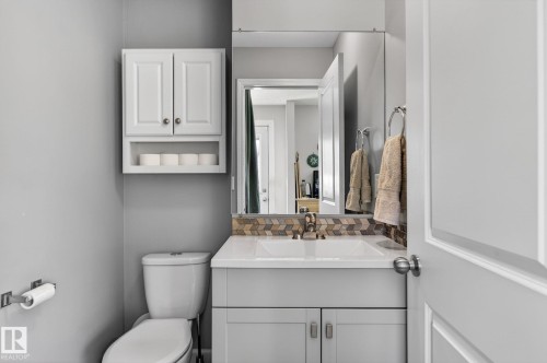 Bathroom featuring a vanity with a white countertop and a chevron tile backsplash, a toilet, and a wall-mounted cabinet with open shelving - 1873 151 Avenue, Edmonton, AB - Indoor Photo Showing Bathroom