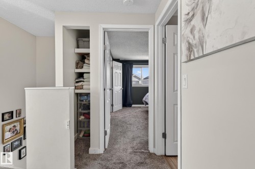 This interior hallway features carpeted flooring and light-colored walls, leading towards a room with a window and curtains - 1873 151 Avenue, Edmonton, AB - Indoor Photo Showing Other Room