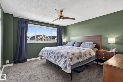 The bedroom features a large window with views of the surrounding properties, plush carpeting, and a ceiling fan - 1873 151 Avenue, Edmonton, AB - Indoor Photo Showing Bedroom
