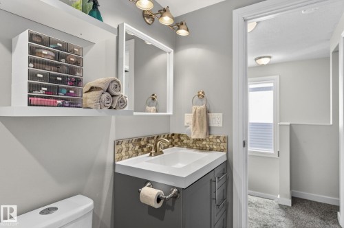 This bathroom features a contemporary vanity with a white countertop and gold-toned faucet, complemented by a decorative tile backsplash - 1873 151 Avenue, Edmonton, AB - Indoor Photo Showing Bathroom