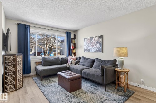 Living area featuring light-toned walls, light wood-style flooring, and a large window with blue curtains - 1873 151 Avenue, Edmonton, AB - Indoor Photo Showing Living Room