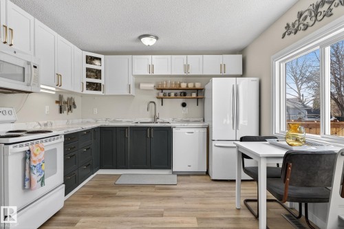 The kitchen features white upper cabinetry with gold hardware, dark lower cabinetry, and a white oven - 1873 151 Avenue, Edmonton, AB - Indoor Photo Showing Kitchen With Double Sink