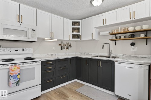 The kitchen features white upper cabinetry, dark lower cabinetry, and a white oven and microwave - 1873 151 Avenue, Edmonton, AB - Indoor Photo Showing Kitchen With Double Sink