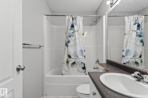 The bathroom features a shower and tub combination, a toilet, and a vanity with a sink and faucet - 30 450 Hyndman Crescent, Edmonton, AB - Indoor Photo Showing Bathroom