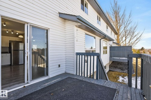 The property features a private deck with dark gray railings and stairs, providing direct outdoor access through a glass sliding door - 30 450 Hyndman Crescent, Edmonton, AB - Outdoor With Exterior