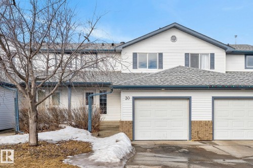 The property features white siding, a gray shingled roof, and an integrated garage with two white garage doors - 30 450 Hyndman Crescent, Edmonton, AB - Outdoor