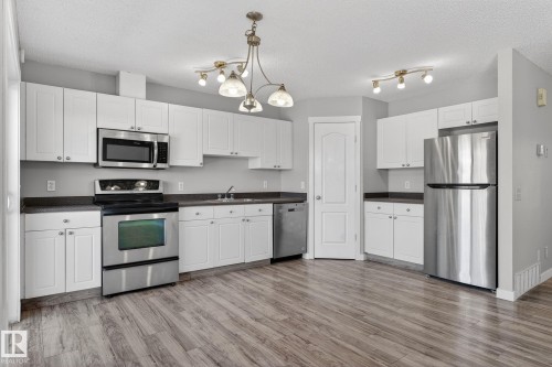 The kitchen features stainless steel appliances, white cabinetry, dark countertops, and wood-look flooring - 30 450 Hyndman Crescent, Edmonton, AB - Indoor Photo Showing Kitchen
