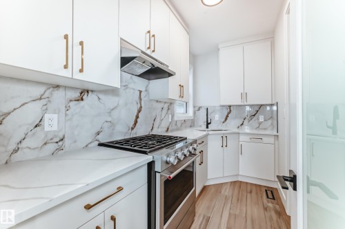 The kitchen features white cabinetry with gold-toned hardware, white countertops, and a white and brown marble-patterned backsplash - 7665 Kimiwan Crescent, Edmonton, AB - Indoor Photo Showing Kitchen With Upgraded Kitchen