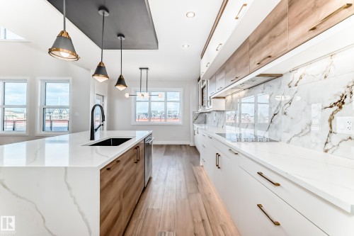 The kitchen features a spacious island with a built-in sink and pendant lighting, complemented by light wood flooring - 7665 Kimiwan Crescent, Edmonton, AB - Indoor Photo Showing Kitchen With Upgraded Kitchen