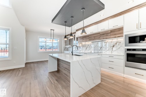 This kitchen features a large island with a waterfall countertop, integrated stainless steel appliances, and a marble-patterned backsplash - 7665 Kimiwan Crescent, Edmonton, AB - Indoor Photo Showing Kitchen With Upgraded Kitchen