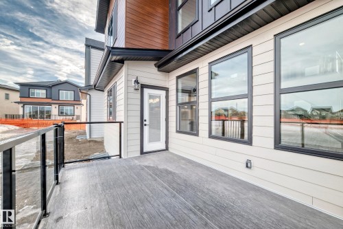 The property features a private deck with glass railings, a white exterior door, and large windows with black frames - 7665 Kimiwan Crescent, Edmonton, AB - Outdoor With Exterior
