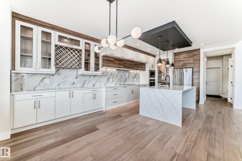 Modern kitchen featuring light hardwood flooring, an island with a waterfall countertop, and white cabinetry - 7665 Kimiwan Crescent, Edmonton, AB - Indoor Photo Showing Kitchen With Upgraded Kitchen