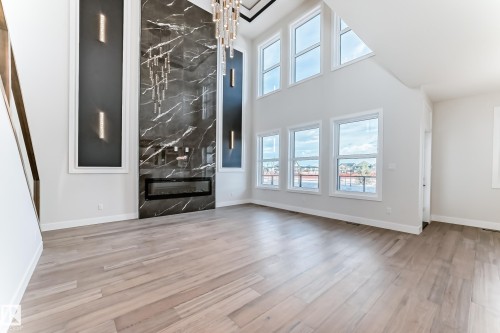 The living area features light-toned wood flooring, a striking black marble-effect fireplace, and tall windows that offer views of the surroundings - 7665 Kimiwan Crescent, Edmonton, AB - Indoor With Fireplace