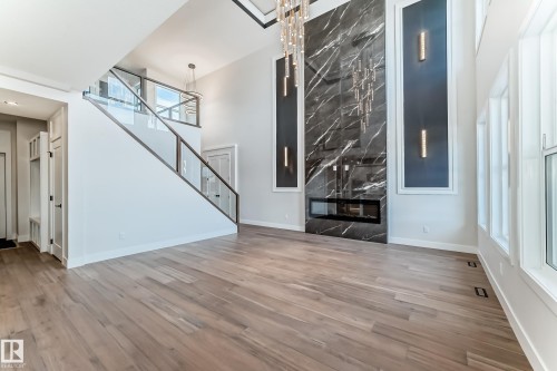 The open-concept living space features light-toned hardwood flooring, a modern fireplace with a black marble surround, and an elegant chandelier - 7665 Kimiwan Crescent, Edmonton, AB - Indoor Photo Showing Other Room With Fireplace