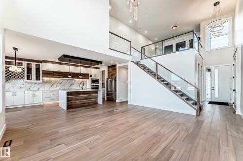 This expansive open-concept main living area features light wood flooring, a contemporary kitchen with a center island, and a prominent staircase with glass railings - 7665 Kimiwan Crescent, Edmonton, AB - Indoor