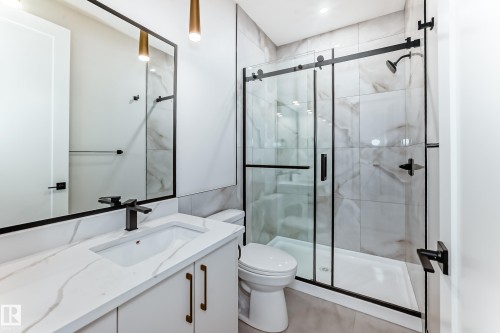 The bathroom features a modern vanity with a white countertop and rectangular sink, a large mirror with a black frame, and a clear glass shower with black framing and fixtures - 7665 Kimiwan Crescent, Edmonton, AB - Indoor Photo Showing Bathroom