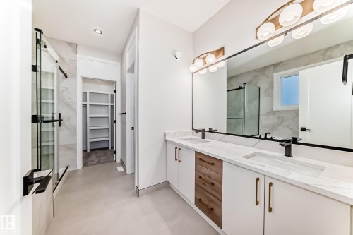 Bathroom featuring a double vanity with white countertops, modern light fixtures, a glass-enclosed shower, and a walk-in closet with shelving - 7665 Kimiwan Crescent, Edmonton, AB - Indoor Photo Showing Bathroom