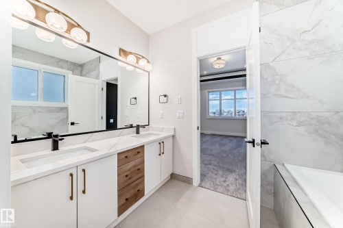 Bathroom featuring a dual vanity with white cabinets, wood drawers, and white countertops, illuminated by two modern light fixtures - 7665 Kimiwan Crescent, Edmonton, AB - Indoor Photo Showing Bathroom