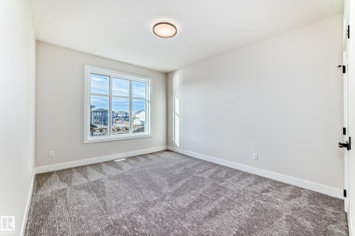 Spacious room featuring light-colored walls, patterned carpeting, and a large window providing natural light - 7665 Kimiwan Crescent, Edmonton, AB - Indoor Photo Showing Other Room