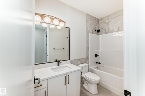The bathroom features a vanity with a white countertop and sink, a mirror with a decorative light fixture, and a bathtub with a shower - 7665 Kimiwan Crescent, Edmonton, AB - Indoor Photo Showing Bathroom