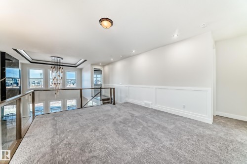 Carpeted loft area with a glass railing overlooking a lower space featuring multiple windows and a chandelier - 7665 Kimiwan Crescent, Edmonton, AB - Indoor Photo Showing Other Room