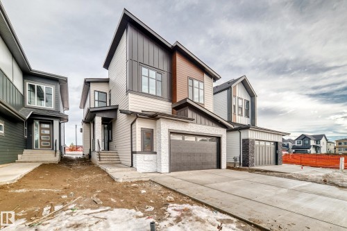 The property features a contemporary architectural style with a prominent dark gray garage door, a light-colored brick facade, and a concrete driveway - 7665 Kimiwan Crescent, Edmonton, AB - Outdoor With Facade
