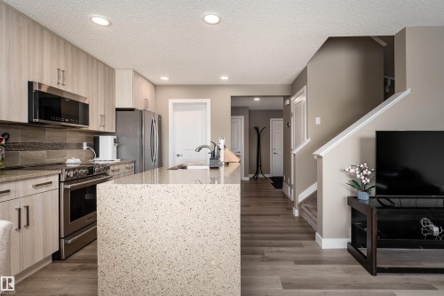 Kitchen featuring light stone counters, stainless steel appliances, a kitchen island with sink, a textured ceiling, and light wood finished floors - 1964 Kroetsch Crescent, Edmonton, AB - Indoor Photo Showing Kitchen With Upgraded Kitchen
