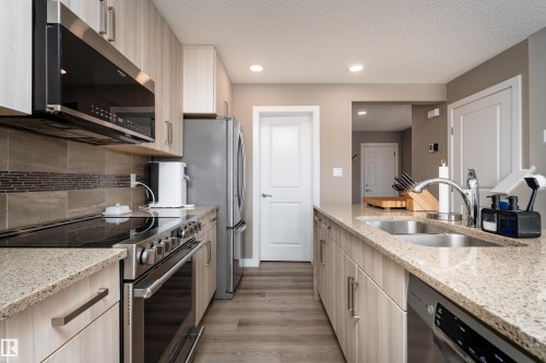 Kitchen featuring stainless steel appliances, light stone counters, light wood finish cabinets, a textured ceiling, and light wood-style flooring - 1964 Kroetsch Crescent, Edmonton, AB - Indoor Photo Showing Kitchen With Double Sink With Upgraded Kitchen