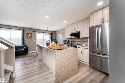 Kitchen featuring stainless steel appliances, light stone countertops, light wood-style flooring, a center island with sink, and a textured ceiling - 1964 Kroetsch Crescent, Edmonton, AB - Indoor Photo Showing Kitchen With Upgraded Kitchen