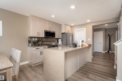 Kitchen featuring light wood-type flooring, light stone countertops, decorative backsplash, stainless steel appliances, and a textured ceiling - 1964 Kroetsch Crescent, Edmonton, AB - Indoor Photo Showing Kitchen