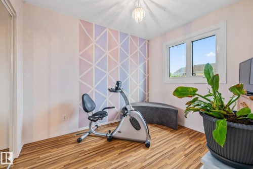 This room features wood-look flooring, a window providing natural light, and a patterned accent wall - 10940 Beaumaris Road, Edmonton, AB - Indoor Photo Showing Gym Room