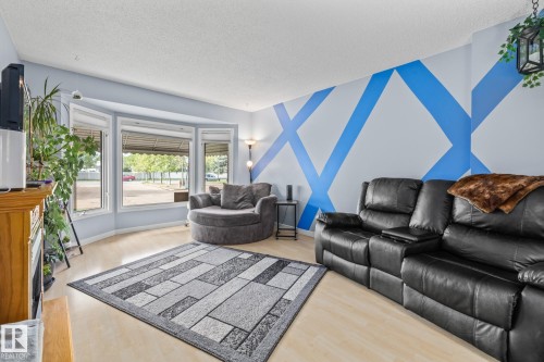 Living area featuring light wood flooring, a decorative wall pattern, and a bay window with a view of mature trees - 10940 Beaumaris Road, Edmonton, AB - Indoor Photo Showing Living Room