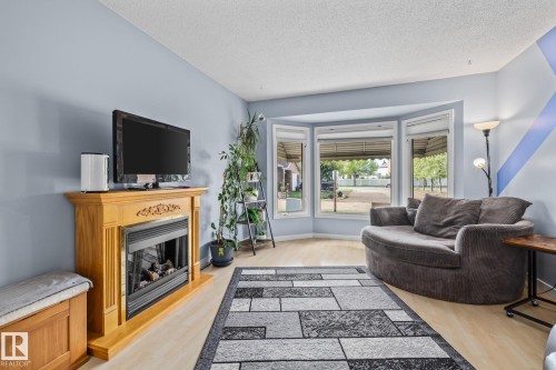 Living area featuring light wood flooring, a fireplace with a light wood mantel, and large bay windows - 10940 Beaumaris Road, Edmonton, AB - Indoor Photo Showing Living Room With Fireplace