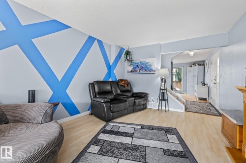 Living area featuring light-colored flooring, a decorative accent wall, and a view towards an entryway with steps - 10940 Beaumaris Road, Edmonton, AB - Indoor Photo Showing Living Room