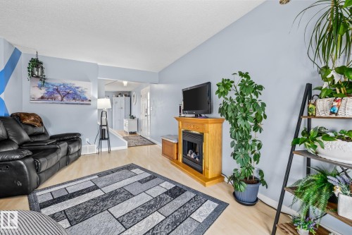 The property features light-toned flooring, light blue walls, and a decorative fireplace with a wooden mantel - 10940 Beaumaris Road, Edmonton, AB - Indoor Photo Showing Living Room With Fireplace