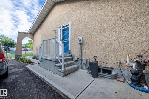 The property features textured exterior walls, a blue door with a storm door, and a concrete entrance with steps and railings - 10940 Beaumaris Road, Edmonton, AB - Outdoor With Exterior