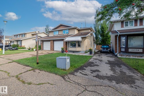 The property features a two-car garage with white doors, a light-colored stucco exterior, and a well-maintained front lawn - 10940 Beaumaris Road, Edmonton, AB - Outdoor With Facade
