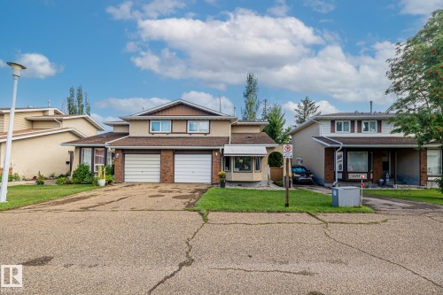 The property features a two-car garage with white doors, a light-colored stucco exterior, and a bay window with a small awning - 10940 Beaumaris Road, Edmonton, AB - Outdoor With Facade