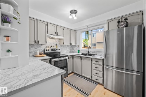 This kitchen features white cabinetry with black hardware, a stainless steel electric range, and a stainless steel refrigerator - 10940 Beaumaris Road, Edmonton, AB - Indoor Photo Showing Kitchen With Stainless Steel Kitchen With Upgraded Kitchen
