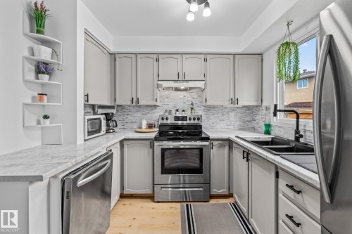 The kitchen features light-toned cabinetry with dark hardware, stainless steel appliances, a white tile backsplash, and light countertops - 10940 Beaumaris Road, Edmonton, AB - Indoor Photo Showing Kitchen With Stainless Steel Kitchen With Double Sink With Upgraded Kitchen