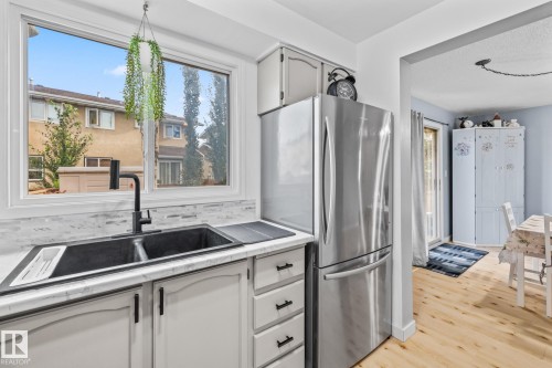 The kitchen features white cabinetry with black hardware, a stainless steel refrigerator, and a double basin sink with a black faucet - 10940 Beaumaris Road, Edmonton, AB - Indoor Photo Showing Kitchen With Double Sink