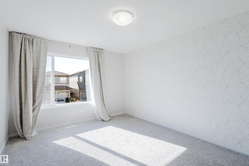 Bright room featuring a large window with drapes, light-colored carpet, a ceiling light fixture, and a wall with textured wallpaper - 2082 Price Landing, Edmonton, AB - Indoor Photo Showing Other Room