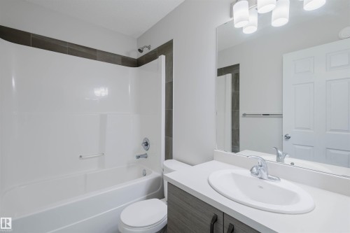 The bathroom features a white bathtub and shower combination with dark tile surround, a white toilet, and a vanity with a white countertop and an oval sink - 2082 Price Landing, Edmonton, AB - Indoor Photo Showing Bathroom